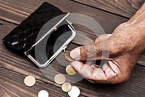 An elderly person holds the coins over the old empty wallet. The