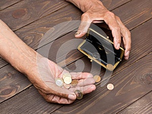 An elderly person holds the coins over the old empty wallet. The concept of poverty in retirement.