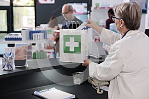 Elderly pharmacist standing at pharmacy counter putting prescription treatment in paper bag