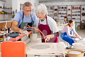 Elderly potter teaches woman how to roll clay on a craft machine clay press roller