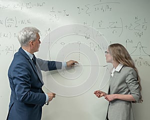 An elderly professor explains a subject to a student at a white board. photo