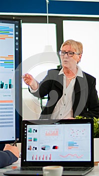 Elderly project manager pointing at desktop presenting statistical data,