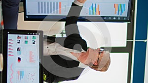 Elderly project manager pointing at desktop presenting statistical data,