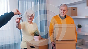 Elderly retired couple buying new home. Woman holding house keys and man carrying cardboard boxes