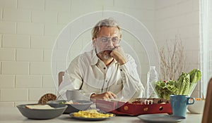 Elderly retired grandfather stay at home with unhappy face sitting alone on eating table in house. Depressed mature Senior old man