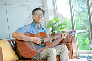 An elderly retired man spends his holidays at home playing the guitar for fun.