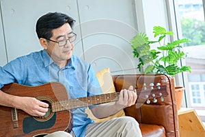 An elderly retired man spends his holidays at home playing the guitar for fun.