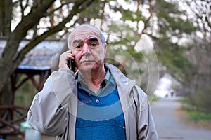 Elderly retired man walking talking on the phone in a city park