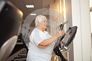 elderly retired woman with gray hair is engaged sports on simulators in gym. Healthy lifestyle, senior concept, indoor