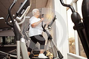 elderly retired woman with gray hair is engaged sports on simulators in gym. Healthy lifestyle, senior concept, indoor