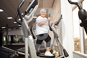 elderly retired woman with gray hair is engaged sports on simulators in gym. Healthy lifestyle, senior concept, indoor