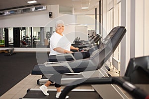 elderly retired woman with gray hair is engaged sports on simulators in gym. Healthy lifestyle, senior concept, indoor