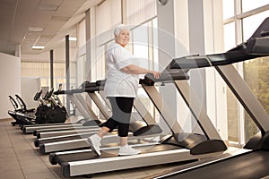 elderly retired woman with gray hair is engaged sports on simulators in gym. Healthy lifestyle, senior concept, indoor