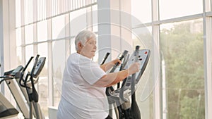 elderly retired woman with gray hair engaged in sports on simulators in gym. Healthy lifestyle, senior concept, indoor