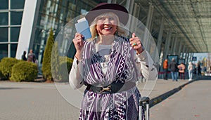 Elderly retired woman tourist near airport terminal celebrating success, winning and goal achievemen