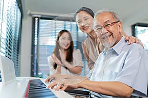 Elderly retirement father sitting on wheel chair playing piano and wife looking at his face in the living room. Daughter caregiver