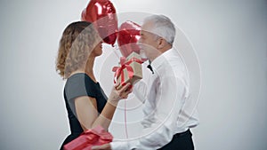 An elderly romantic couple  an attractive woman and a man with balloons in their hands give each other gifts.