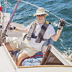 An elderly seafarer manages a sailing boat on a sunny summer day.
