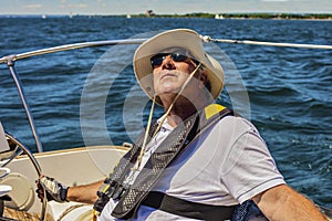 An elderly seafarer manages a sailing boat on a sunny summer day.