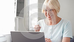 Elderly senior blond woman working on laptop computer at home. Received good news excited and happy