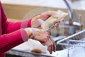 Elderly senior lady applying hand cream to old wrinkled cracked dry hands to moisturise for skin care