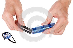 Elderly senior man inserts  AAA sizes  batteries  into a in  LED compact flashlight isolated