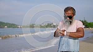 Elderly senior runner man with grey beard checks health state, uses modern fitness tracker watch wearable gadget, does