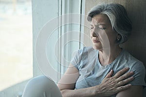 Elderly senior sick disabled, sad woman in pain and suffering sitting by the window in the hospital.