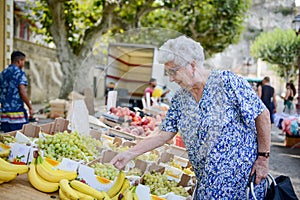 Elderly senior woman buying fresh vegetables and fruits in farmer`s market during summer day in provence france