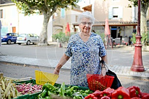 Elderly senior woman buying fresh vegetables and fruits in farmer`s market during summer day in provence france