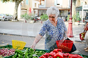 Elderly senior woman buying fresh vegetables and fruits in farmer`s market during summer day in provence france