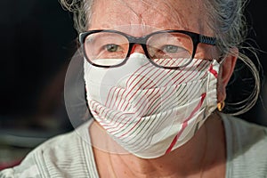 Elderly senior woman with glasses wearing hand made cotton mouth nose virus face mask. Coronavirus covid-19 outbreak prevention