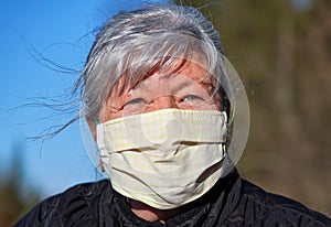 Elderly senior woman with gray hair wearing home made cloth face mouth nose virus mask outside. Can be used during coronavirus