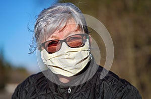 Elderly senior woman with gray hair wearing home made cloth face mouth nose virus mask outside. Can be used during coronavirus