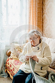 Elderly senior woman with grey hair knitting scarf. Old retired female. Aged wife in cozy home sweater. Elder pensioner