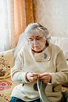 Elderly senior woman with grey hair knitting scarf. Old retired female. Aged wife in cozy home sweater. Elder pensioner