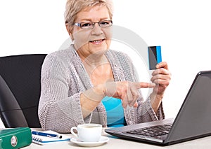 Elderly senior woman holding credit card and showing laptop screen, paying over internet for utility bills or shopping