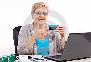 Elderly senior woman holding credit card and showing thumbs up, paying over internet for utility bills or shopping