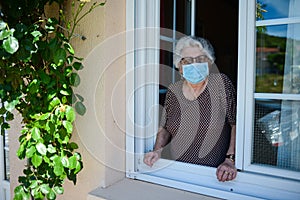 Elderly senior woman opening a window house and welcoming people at home wearing a surgical mask covid19