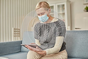 An elderly senior woman in a protective mask holding a tablet in her hands. Coronavirus covid-19 outbreak prevention concept