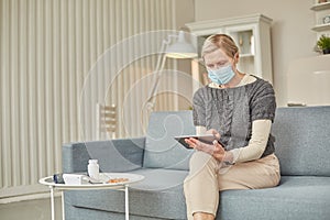 An elderly senior woman in a protective mask holding a tablet in her hands. Coronavirus covid-19 outbreak prevention concept