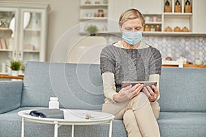 An elderly senior woman in a protective mask holding a tablet in her hands. Coronavirus covid-19 outbreak prevention concept