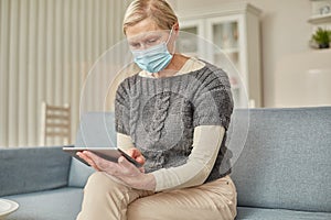 An elderly senior woman in a protective mask holding a tablet in her hands. Coronavirus covid-19 outbreak prevention concept