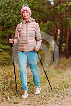 Elderly sixty-year-old woman in sportswear is engaged in Nordic walking with sticks in the forest in the autumn