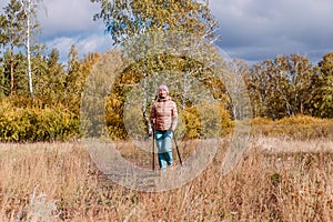 Elderly sixty-year-old woman in sportswear is engaged in Nordic walking with sticks in the forest in the autumn