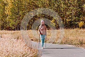 Elderly sixty-year-old woman in sportswear is engaged in Nordic walking with sticks in the forest in the autumn