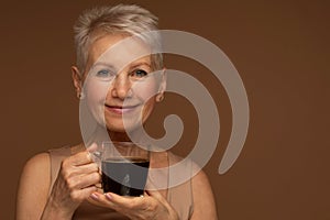 Elderly smiling fashionable positive happy blonde caucasian woman hold a mug of coffee