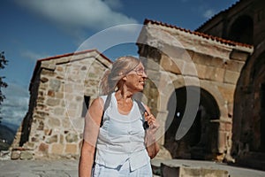 Elderly smiling senior traveling woman backpacker tourist walking posing outdoors in ancient Europe fortress ruins