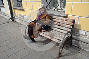 Elderly smiling woman sits on bench in coat and hat in spring city