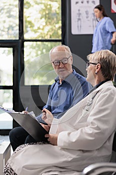 Elderly specialist doctor holding clipboard showing medical expertise to old man patient discussing illness diagnosis